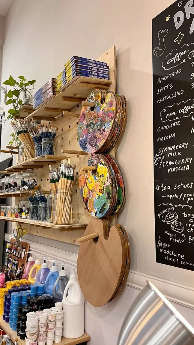 Estante del taller con pinceles, paletas usadas y botes de pintura ordenados.